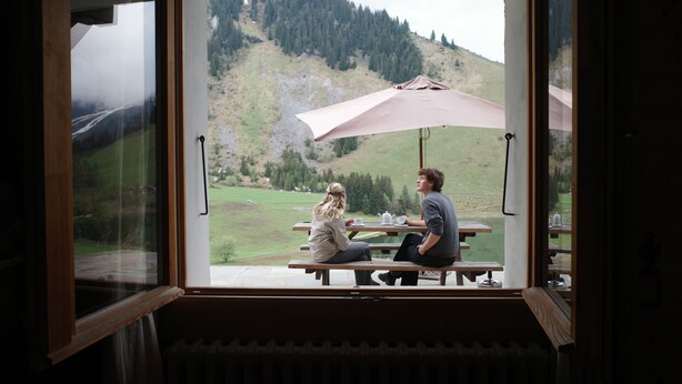 A room with a large window, a wooden bench, and a picnic table. - Charming Apartment for Rent - Log Cabin - Directly on Lake des Confins - Sleeps 8 (La Clusaz)