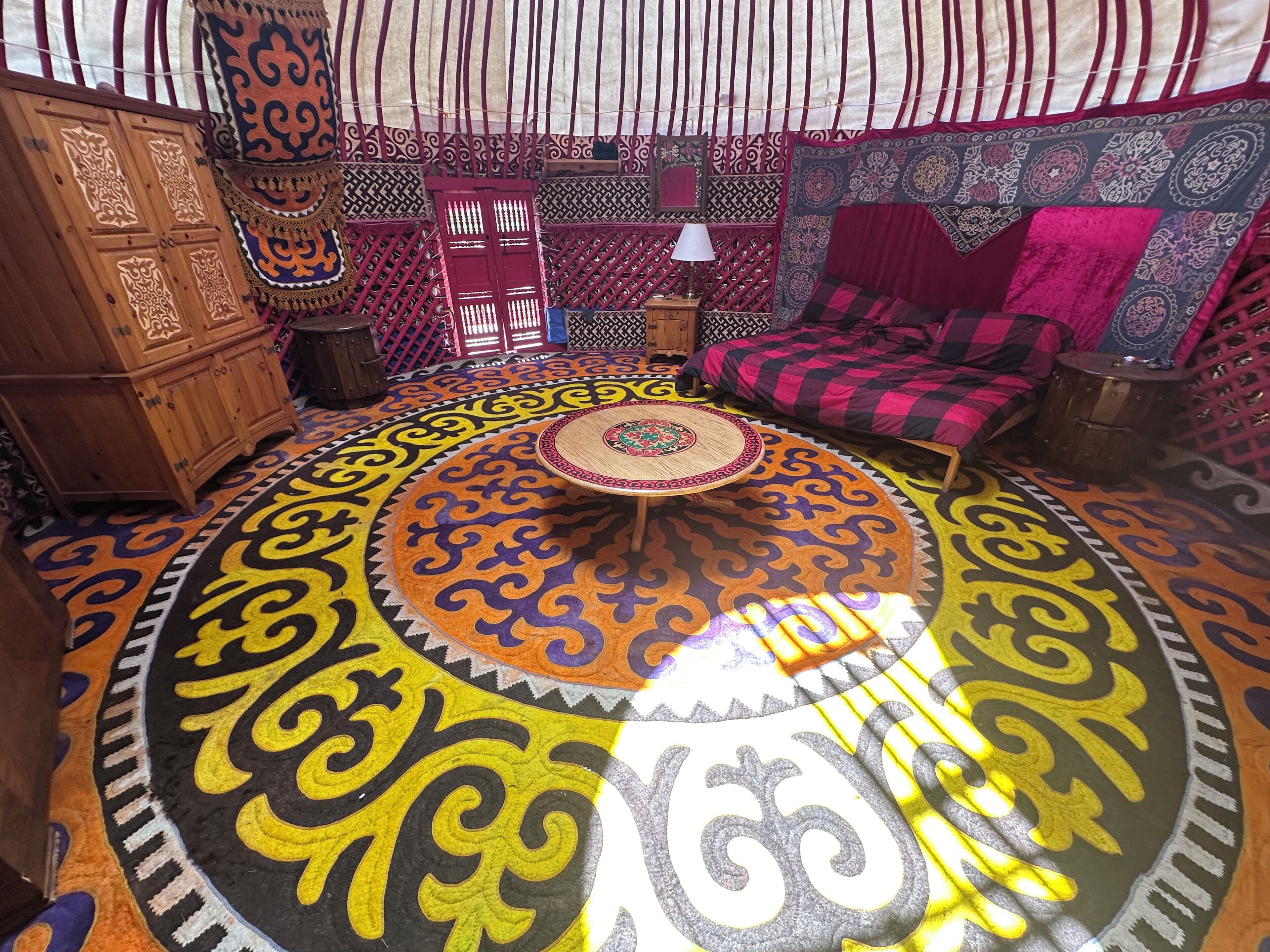 A room with a patterned floor, a wooden cabinet, a round table, and a sofa with a patterned blanket.