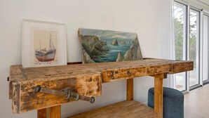 Un tavolo in legno rustico con un manico metallico, un quadro incorniciato raffigurante una nave e vista sul mare attraverso una porta in vetro.