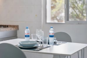A dining table with clear glasses, plates, and water bottles, set against a white wall and a window with a view of trees. - Charming 1-bedroom Apartment With Ocean View in Arona (Arona)