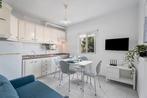 A compact kitchen with white cabinets, a dining table with chairs, a TV mounted on the wall, and a blue sofa in the living area. - Charming 1-bedroom Apartment With Ocean View in Arona (Arona)