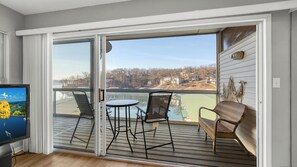 Ein Balkon mit Tisch und Stühlen, einem Fernseher und Blick auf einen See sowie Gebäude.