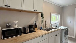 A modern kitchen with white cabinets, a wooden countertop, a microwave, a coffee maker, and a stove.