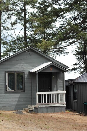 Une petite cabane à un seul étage, dotée d’un porche, d’une porte bien visible et du chiffre « 7 » sur la façade.