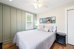 A bedroom with a bed, a nightstand, a ceiling fan, a window with blinds, and wall art. - Tour MQT, NMU - Comfy UP Getaway - Full Amenities - 1 Bed (Marquette)