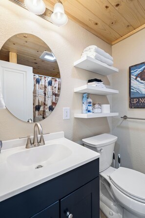 A bathroom with a white sink, a toilet, and a mirror. There are shelves above the toilet with towels and toiletries. - Tour MQT, NMU - Comfy UP Getaway - Full Amenities - 1 Bed (Marquette)