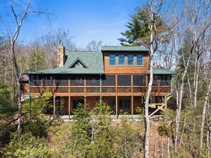 A two-story log cabin with a green roof, multiple windows, and a stone chimney. - Blue Ridge Escape with Stunning Views, Fenced Yard & EV Charger (Blue Ridge)