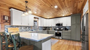 Cocina moderna con techo de madera, armarios blancos, electrodomésticos de acero inoxidable e isla central con taburetes de bar.