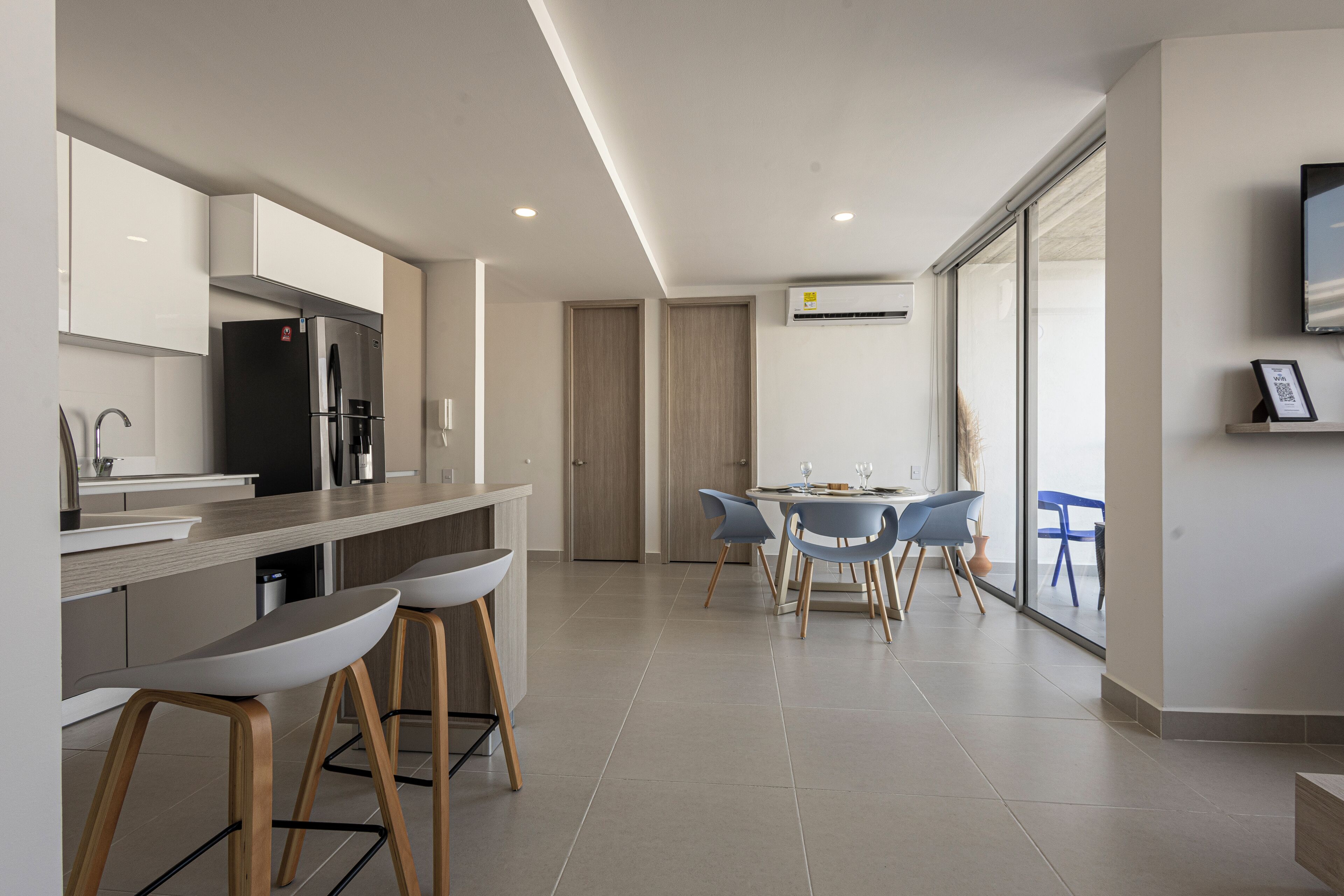 Una cocina moderna con refrigerador integrado, una zona de comedor con mesa y sillas, y un ventanal que ofrece vistas al exterior.