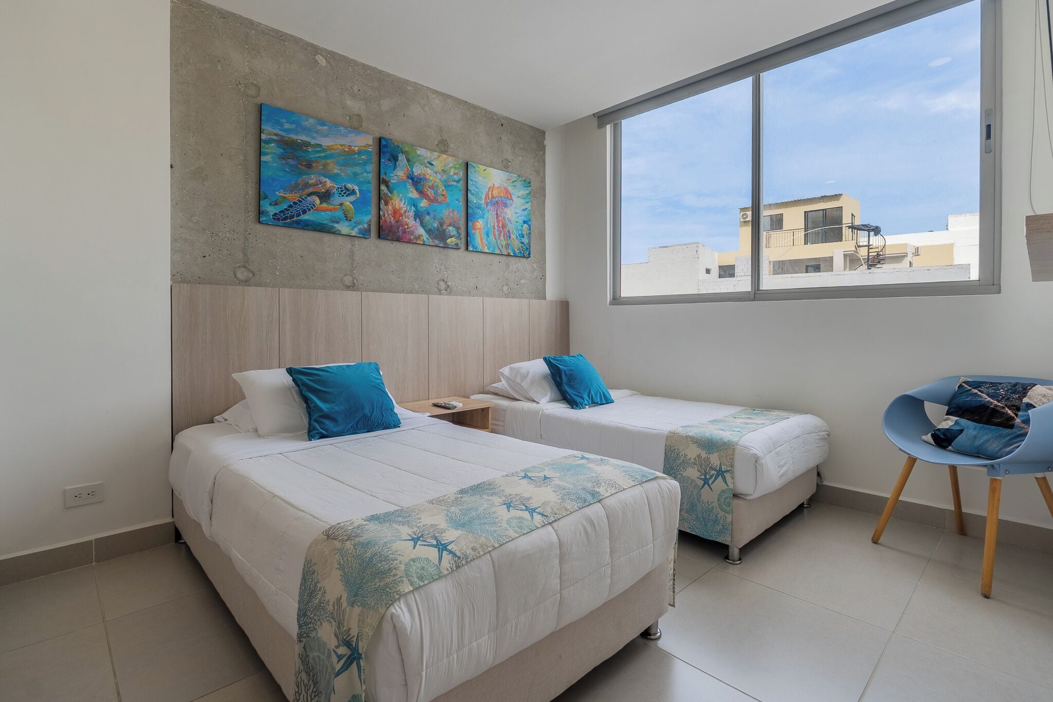 Habitación de hotel con dos camas, un ventanal grande y obras de arte en la pared.