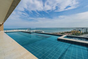 Une piscine à débordement située sur le toit, offrant une vue dégagée sur l’océan et le paysage urbain.