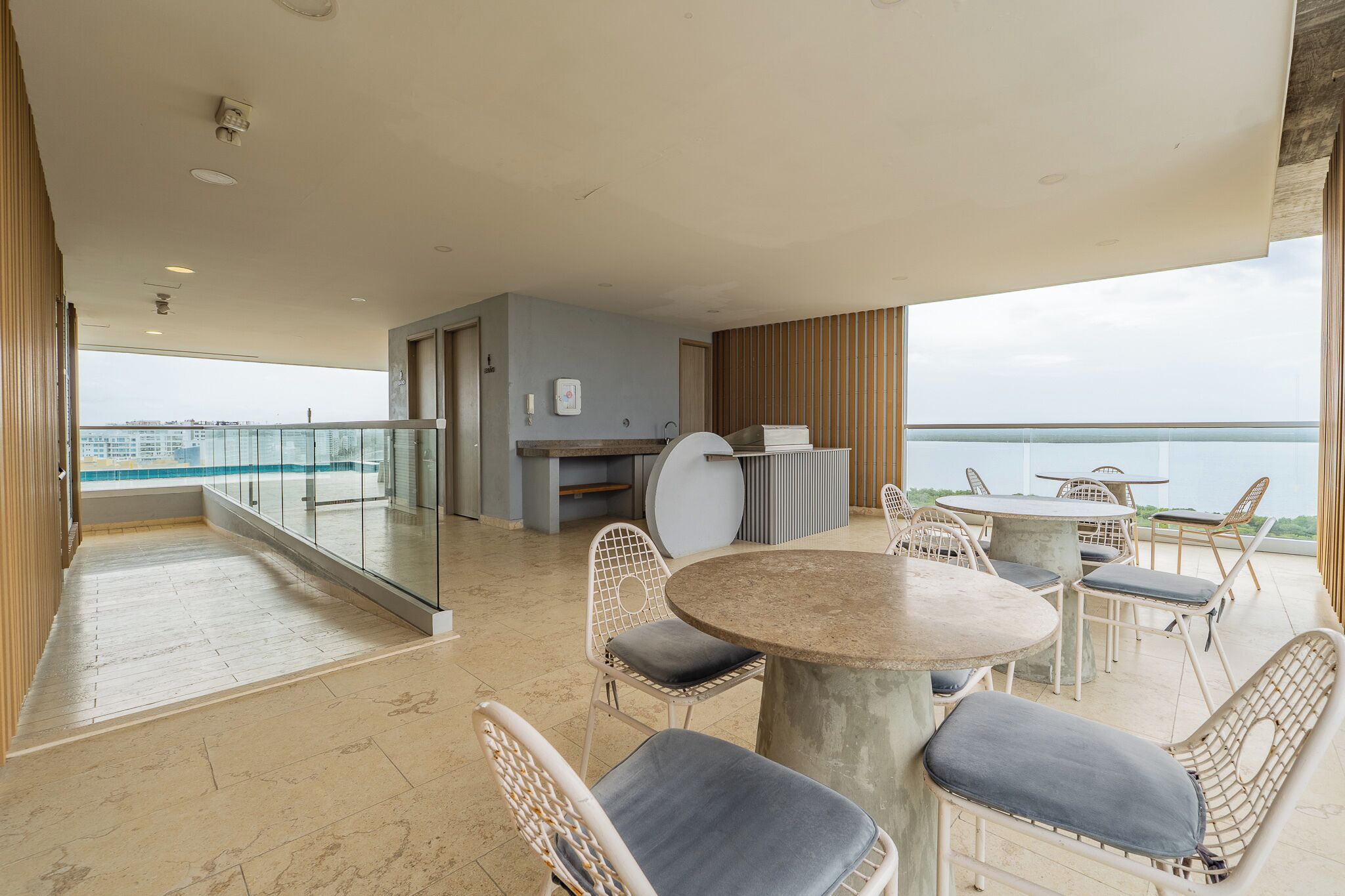 Un balcón con mesa y sillas, vista al mar y barandilla de vidrio.