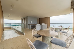Un balcon avec une table et des chaises, une vue sur la mer et une rambarde en verre.