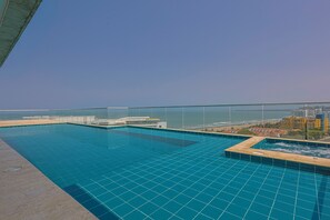 Une piscine à débordement située sur le toit, offrant une vue dégagée sur l’océan et les bâtiments en arrière-plan.