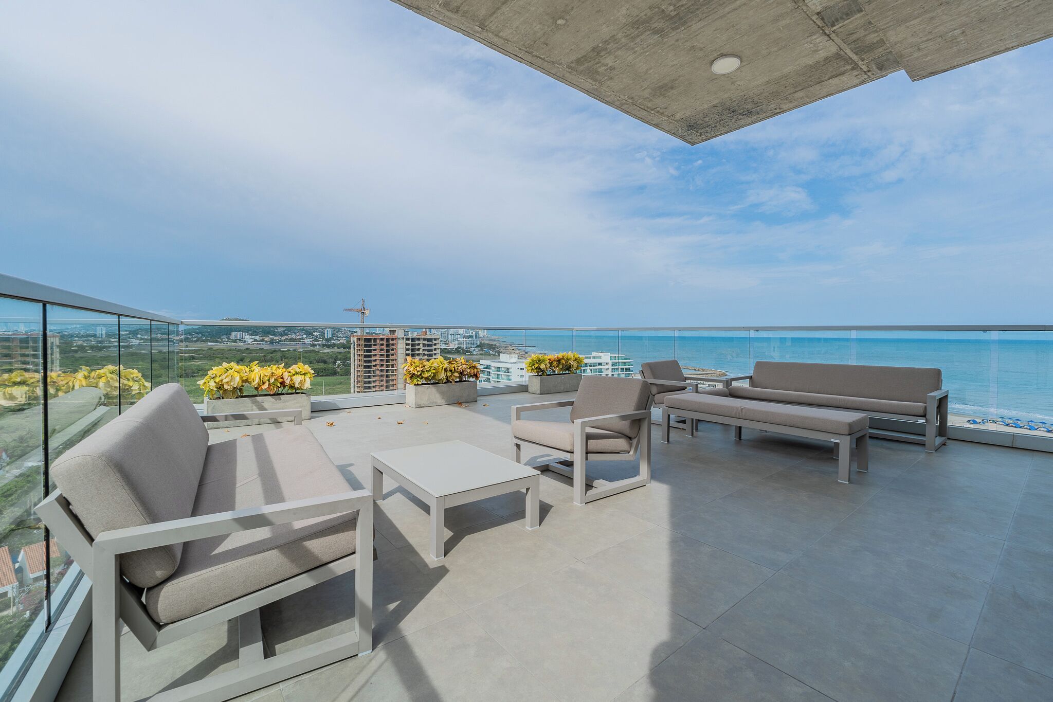 Una terraza en la azotea con mobiliario exterior, vista al océano y una grúa de construcción al fondo.