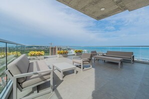 Une terrasse sur le toit, aménagée avec du mobilier d’extérieur, offrant une vue sur l’océan et, au loin, une grue de chantier.