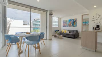 A modern living room with a gray sofa, a coffee table, and a dining area with blue chairs.