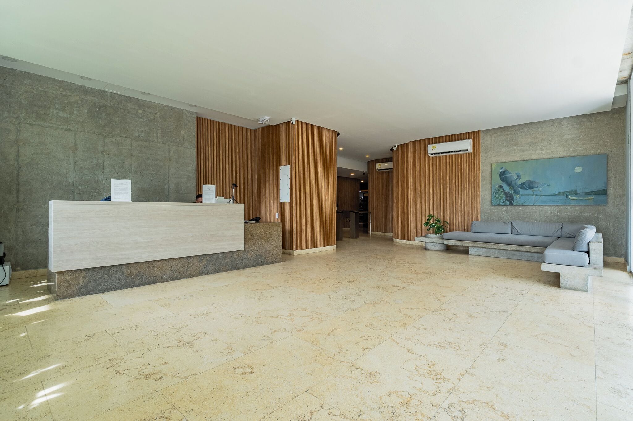 Un área de recepción con un mostrador de madera, un sofá gris y un cuadro en la pared.