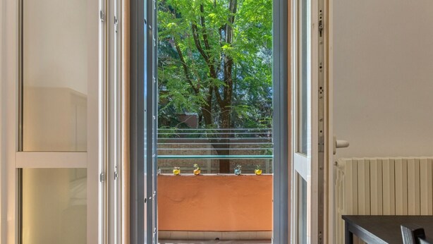 An open door leading to a balcony with a view of trees and a railing with potted plants.