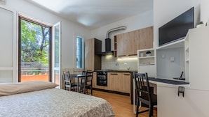 A compact room with a bed, a dining table, a kitchen area, and a TV.