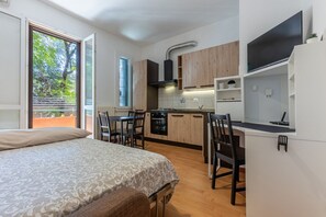 A compact room with a bed, a dining table, a kitchen area, and a TV.