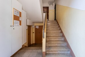 Eine Treppe mit Handlauf, ein Schwarzes Brett mit Aushängen und eine Tür am oberen Ende.