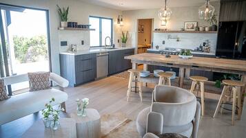 Una cocina moderna con una isla central, taburetes de bar y un área de comedor con sofá y mesa de centro.