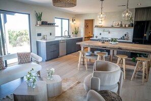 A modern kitchen with a central island, bar stools, and a dining area with a sofa and coffee table. - Wellness Farm Retreat on 19 Acres with Gym, Sauna, Hot/Cold Plunge + Donkeys (Bonsall)