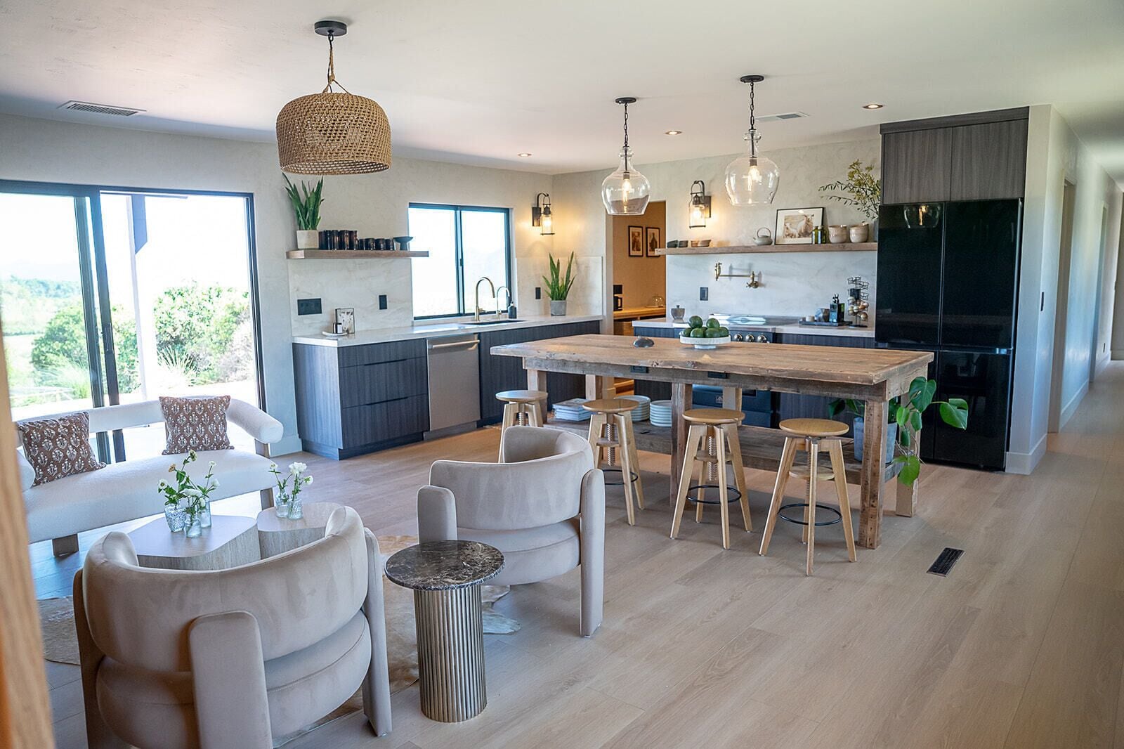 Una cocina moderna con una isla central, taburetes de bar, iluminación colgante y un ventanal amplio.