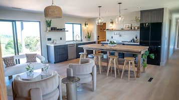 Una cocina moderna con una isla central, taburetes de bar, iluminación colgante y un ventanal amplio.