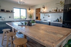 A kitchen with a large island, bar stools, a stove, and a large window. - Wellness Farm Retreat on 19 Acres with Gym, Sauna, Hot/Cold Plunge + Donkeys (Bonsall)