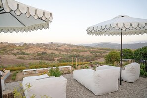 An outdoor seating area with white cushioned chairs and tables, white umbrellas, and a scenic view of rolling hills and mountains. - Wellness Farm Retreat on 19 Acres with Gym, Sauna, Hot/Cold Plunge + Donkeys (Bonsall)