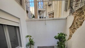 Un pequeño balcón con zona de estar, plantas en macetas y vistas a edificios cercanos.