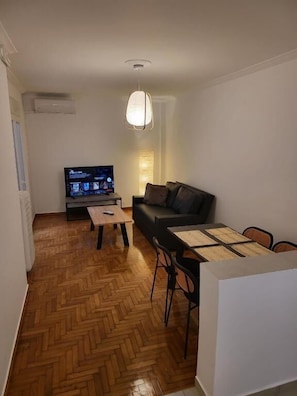 Ein Wohnzimmer mit einer Couch, einem Couchtisch, einem Fernseher und einem Esstisch mit Stühlen.