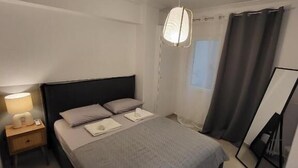 Un dormitorio moderno con cama, mesita de noche, lámpara y cortinas.