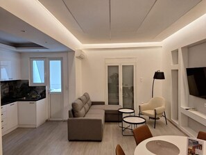 Ein modernes Wohnzimmer mit einer Couch, zwei kleinen Tischen, einem Sessel und einem Fernseher.