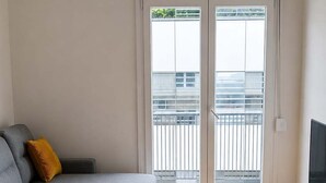 Een woonkamer met een grijze bank, een houten salontafel, een televisie op een standaard, en een glazen schuifdeur die uitkomt op een balkon.