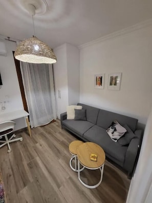Un salon moderne avec un canapé gris, une table basse en bois, un luminaire suspendu et un bureau blanc.