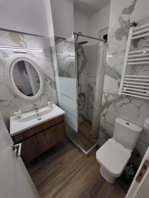 Une salle de bain moderne avec une douche à parois de verre, des toilettes blanches et un mur recouvert de carreaux de marbre.
