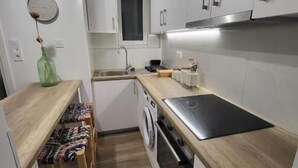 A compact kitchen with white cabinets, a wooden countertop, a built-in oven, and a washing machine. - Stay Now at Acropolis (Athina)