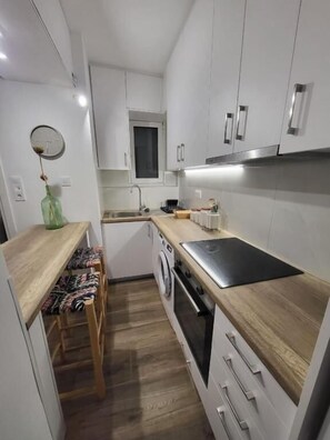 Eine kleine Küche mit weißen Schränken, einer Holzausziehtafel, einem Einbauofen und einer Waschmaschine.