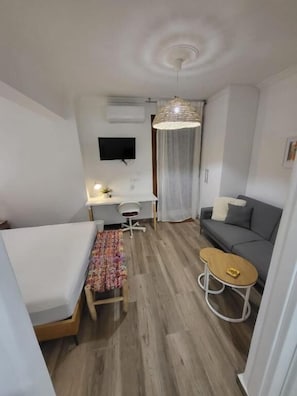 Une pièce de taille modeste comprenant un lit, un bureau, un canapé, une petite table et un luminaire suspendu.