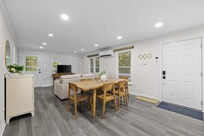 A dining area with a wooden table and chairs, a sofa, a TV, and a white brick wall. - Lake Anna Cottage w Hot Tub, Kayaks & Boat Launch (Mineral)
