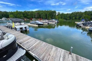 A wooden dock with boats docked, a clear sky, and a forested shoreline.