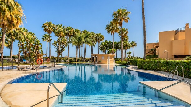Ein Swimmingpool mit Palmen, Liegestühlen und einem kleinen Gebäude.