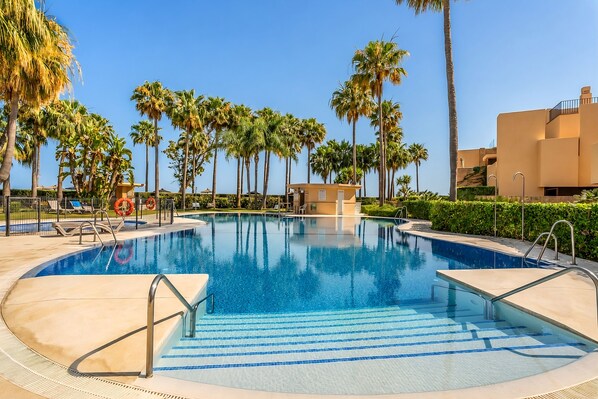 Ein Swimmingpool mit Palmen, Liegestühlen und einem kleinen Gebäude.
