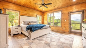 Ein Schlafzimmer einer Holzhütte mit Bett, Nachttischen und großen Fenstern.