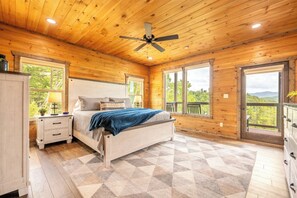 A wooden cabin bedroom with a bed, nightstands, and large windows. - 🏔️ Redtail Horizon | Indoor Pool, Hot Tub + Mountain Views🏔️ (Sevierville)