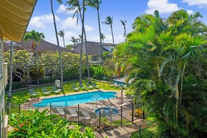 Piscina cercada por palmeiras e um deck com grade.