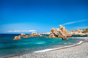 Ein felsiger Strand mit klarem türkisfarbenem Wasser und blauem Himmel.